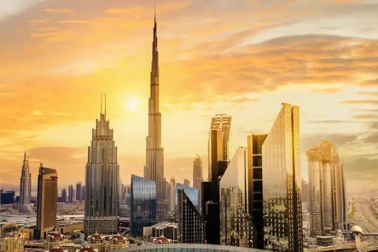 Sunset view of Dubai skyline featuring the Burj Khalifa surrounded by modern skyscrapers, reflecting golden sunlight under a dramatic orange sky.
