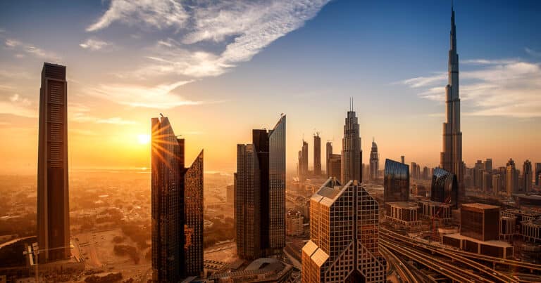 Sunset skyline of Dubai featuring the Burj Khalifa and modern skyscrapers, with golden sunlight illuminating the city’s architecture and roads below.
